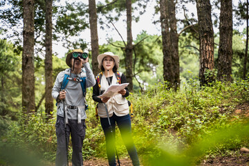 Bird watching man using binocular and woman holding map hiking in the woods