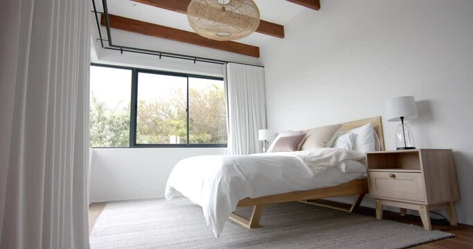 Interior of domestic bedroom with double bed and window overlooking garden, copy space, slow motion