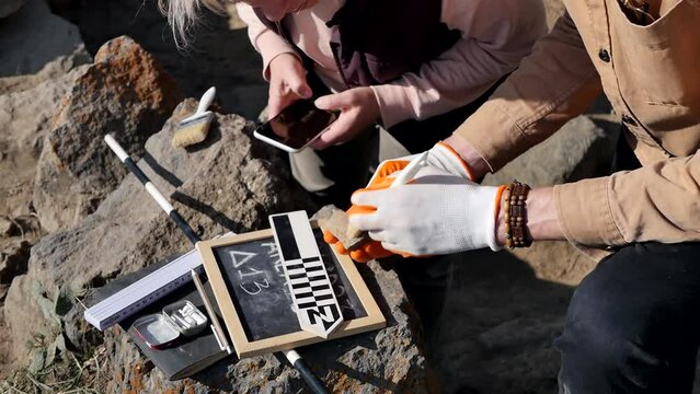 Archaeological excavations. Two archaeologists use archaeological excavation tools to clean dust from found artifacts and take pictures using a smartphone. Scientists explore historical finds