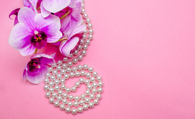 Pearl necklace and purple orchid on pink background
