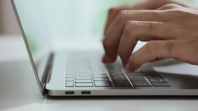 The man's hand is typing on a laptop computer keyboard at home or in the office. He is working, sending messages, chatting, browsing the internet, and using social networking.