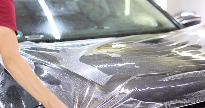 Man repairman wrapping protective vinyl film over car 4k movie. Auto detailing and service concept