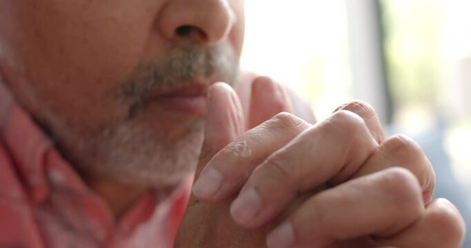 Close up of worried senior biracial man sitting with hands clasped in living room, slow motion