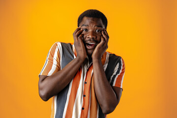Surprised african stylish young man in striped shirt against yellow background