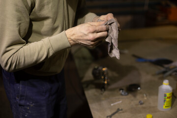 Wipe part with rag. Rag in his hands. Person cleans mechanism from dirt.