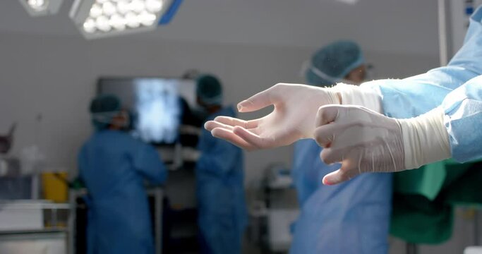 Midsection of african american surgeon wearing surgical gloves in operating theatre, slow motion