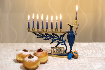 Menorah (Chanukkia) with 8 lit burning candles for Jewish Hanukkah holiday on table at home. Celebrating Chanukah festival of lights. Dreidel and Sufganiyot donuts sweet cultural food on a plate. 