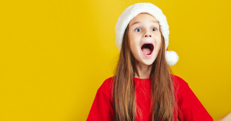 Little surpised kid girl 7-8 years old wear Santa hat say wow isolated on bright yellow background...