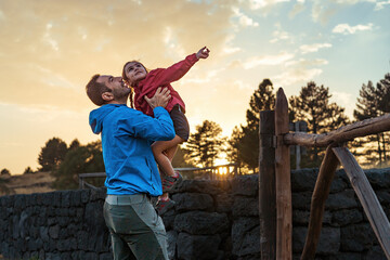 Father playfully lifting his daughter as they enjoy a sunset together, capturing a joyful moment of...