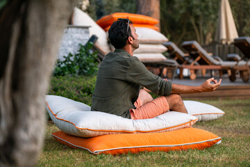 Young man meditates in a nature-themed hotel. Young man meditating and relaxing on a white and orange floor cushion.