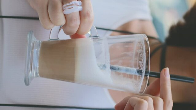 vertical shot. close-up of a glass of latte. The girl holds a glass of latte and drinks it through a straw.