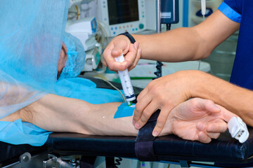 An anesthesiologist injects intravenous anesthesia with a large syringe into the patient's arm on the operating table. Surgery with general anesthesia.