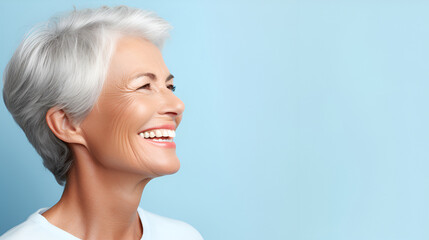 Portrait of a beautiful smiling senior woman with gray hair and white perfect teeth isolated on a blue studio background with copy space. Dental care. Dental prosthetics. Dentistry concept.