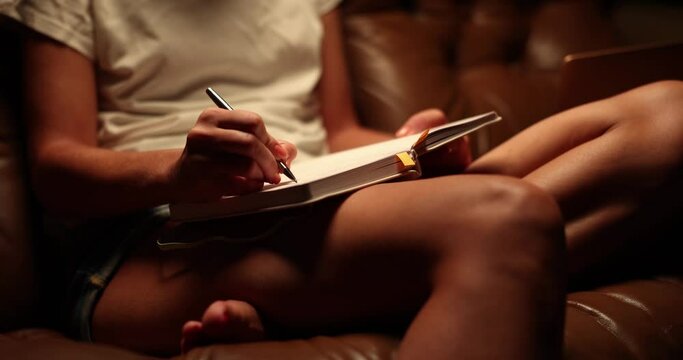 Woman is sitting on couch writing notes or planning tomorrow evening. Evening entries in diary