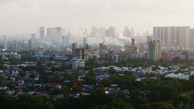 Mumbai suburban cityscape with buildings, factories with smoke chimneys, slums and metro rail passing. Indian city with factories close to residential buildings polluting the air.