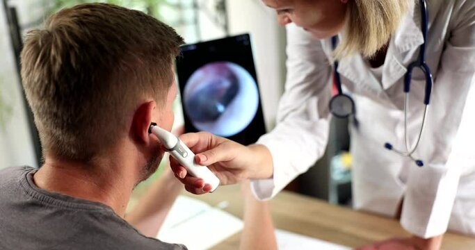 Adult male during ear examination at hearing clinic. Audiologist examining ear of male patient with digital otoscope with image on screen closeup