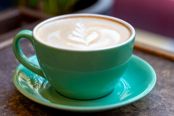 Fresh tasty aromatic coffee latte with pattern in green ceramic cup on table close-up. Delicious breakfast. Selective focus