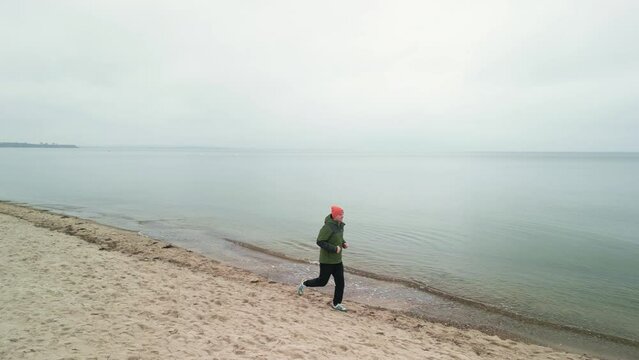 Ein junger Mann rennt an einem bewölkten Tag am Strand entlang. Ein Mann läuft am Sand entlang.