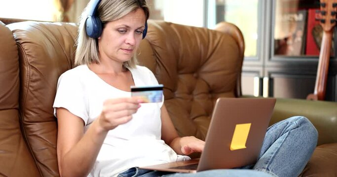 Woman in headphones and with bank card pays for language courses online on a laptop. Remote payment and ordering goods on Internet