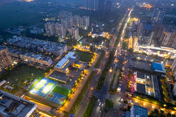 aerial drone shot showing brightly lit street with multi story sky scrapers offices, homes, shopping malls, sports arenas and more in metropolitan city like gurgaon, delhi, mumbai, bangalore