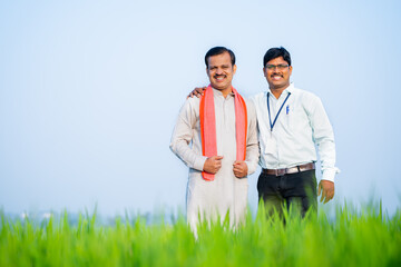 wide shot of Happy supportive banker with village farmer standing by looking at camera near green...