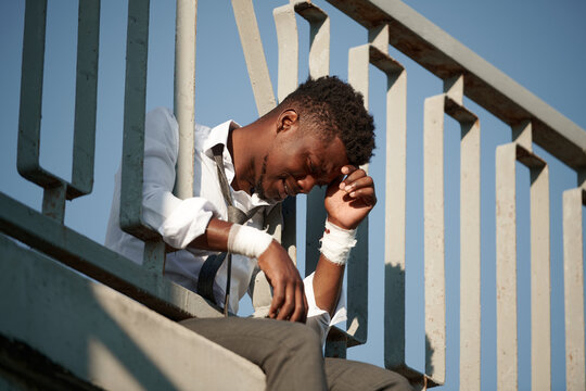 African American worried man sitting on the edge of bridge with bandaged wrists and crying
