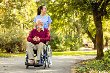Nurse and elderly man in wheelchair going for a walk in the park.