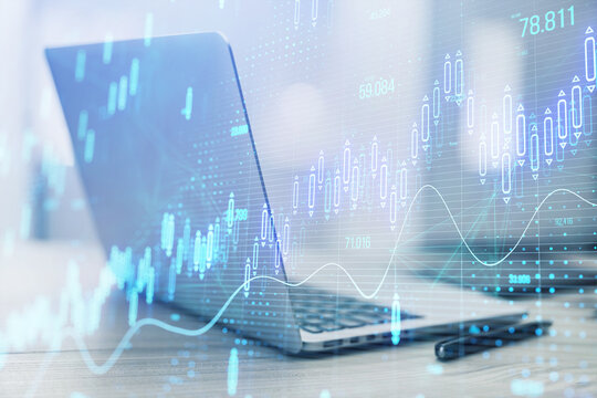 Close up of laptop computer on desk with glowing candlestick forex chart on blurry background. Stock market, trading analysis and investment concept. Toned image. Double exposure.