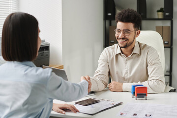 Smiling specialist shaking hands with tourist in visa center during their interview