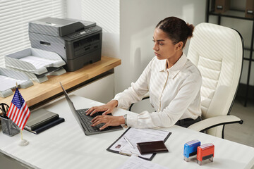 Businesswoman sitting at her workplace and typing data of documents in laptop
