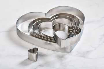 Set of stainless steel heart-shaped cookie cutters on a white marble surface