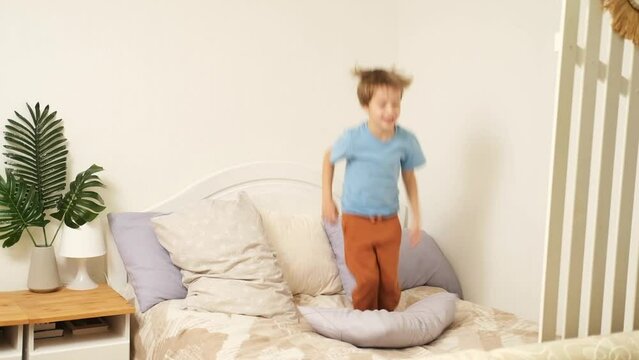 Funny adorable happy kid boy jump and dance on bed in the morning. Happy holidays and new day concept.