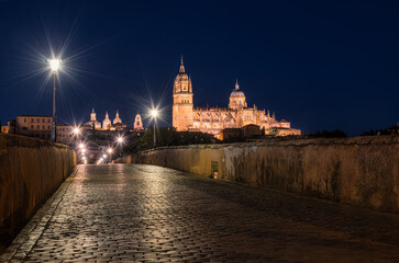 Nighttime view of The Salamanca Roman Bridge (Puente Romano de Salamanca, Puente Mayor del Tormes), ancient stone structure over the Tormes River with Salamanca Cathedral in the background