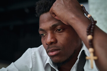 African American upset young man with rosary beads thinking about his problems