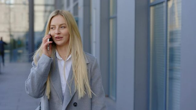 Portrait of Fashionable Blonde Lady Walking Outside, Speaking on a Smartphone. Chic Attractive Urban Businesswoman Conversing on a Cellphone. Phone Conversation. Business and Technology Concept
