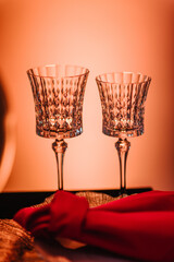 Fototapeta na wymiar Two glasses closeup, red linen napkin, golden plate, silverware cutlery, fork. Serving guests, setting table. Served banquet. Wedding set up. Side view. Luxury reception for birthday party.