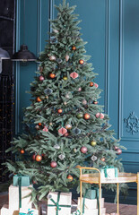 Stunning Christmas tree with decorations for Christmas and New Year. Table with gifts. Background - blue wall. Festive design. Holidays concept