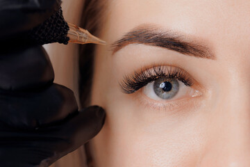 Procedure Permanent makeup tattoo for eyebrows. Detail of beautiful woman with black brows in...