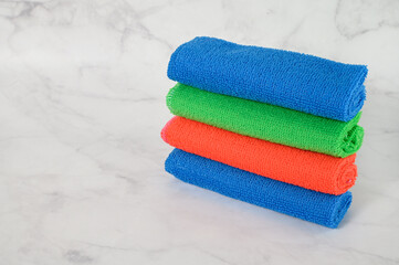 Stack of multicolored microfiber cloths on a light marble background. Space for text.
