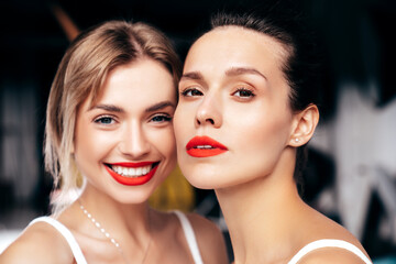 Closeup portrait of two young beautiful smiling brunette female with glamour evening makeup. Sexy women with healthy glowing face skin. Hot models with red lips posing over dark background