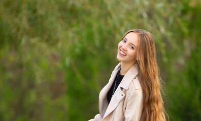 A young smiling girl walking in an autumn park in a good mood. Teenage girl, portrait against a background of nature. Fashion style trend.