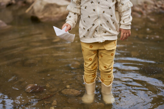 Girl holding paper boat and standing in water puddle