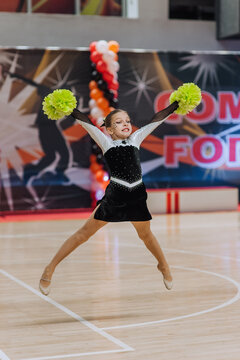 Professional athlete, girl cheerleader with green pom-poms dances, jumps in the gym at a cheerleading competition. Photography, portrait, sport concept. MyRealHoliday.