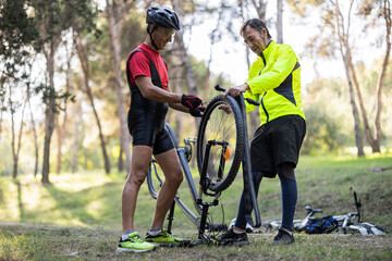 Mature friends repairing tire of bicycle in forest