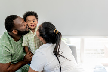 African family, Nigerian father, Asian mother holding and kissing a 10-month-old baby newborn son, they are smile and happy together. to African family and baby infant concept.