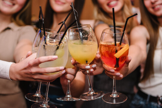 Happy young people cheering drinks at bar restaurant. Toasting, summer colorful cocktails. Cheers with glasses at pub. Party time concept. Group of friends partying in nightclub. Side view of hands up