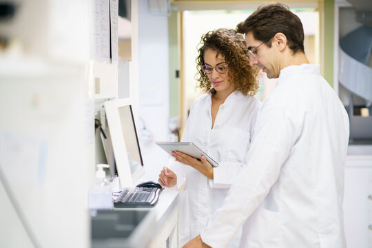 Pharmacist working with colleague using tablet PC at pharmacy - Powered by Adobe