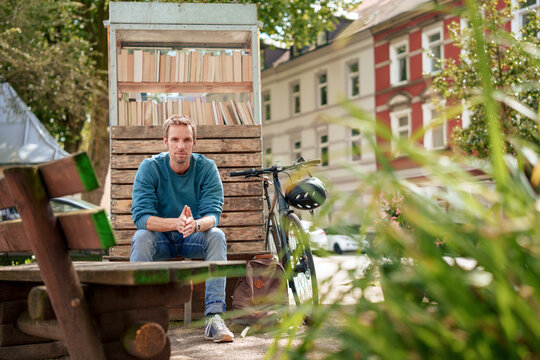 Man sitting on bench near cabinet of books near plants