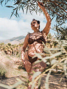 Beautiful woman wearing bikini touching branch of tree in park
