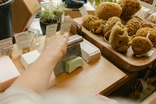 Hand of woman owner cutting bar of soap on table in store